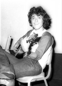 Young Shlomo Artzi seated with a guitar