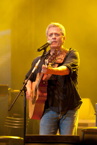 Shlomo Artzi singing and playing guitar under stage lighting